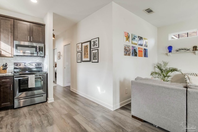 kitchen with decorative backsplash, appliances with stainless steel finishes, light stone countertops, dark brown cabinetry, and light hardwood / wood-style floors