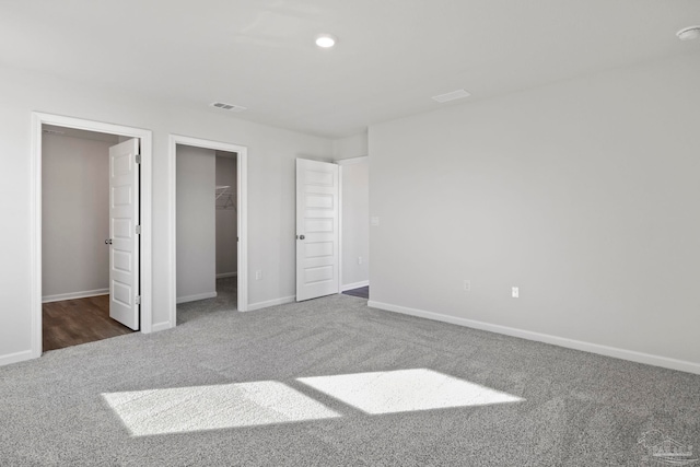 unfurnished bedroom with a walk in closet, carpet flooring, visible vents, and baseboards