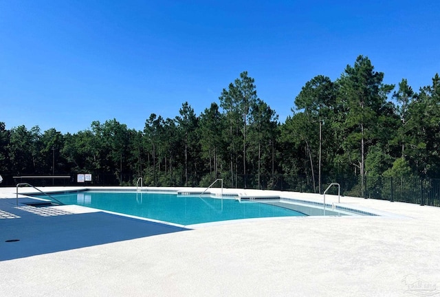 pool featuring a wooded view, fence, and a patio