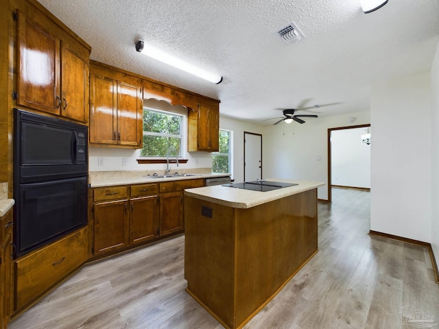 kitchen with light wood-type flooring, sink, a center island with sink, and black appliances