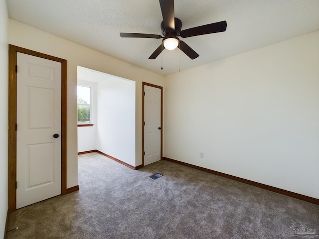 unfurnished bedroom with ceiling fan, a textured ceiling, and dark carpet