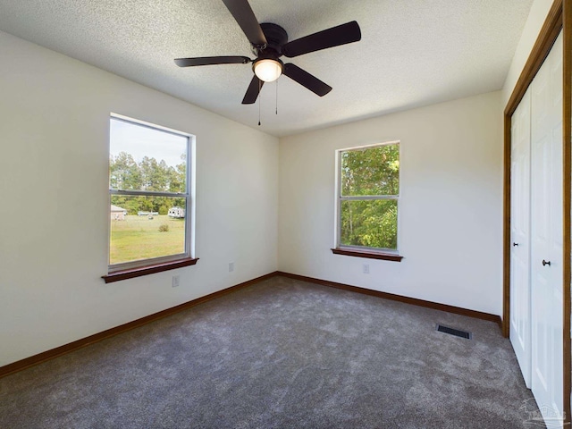 unfurnished bedroom with a closet, a textured ceiling, multiple windows, and dark colored carpet