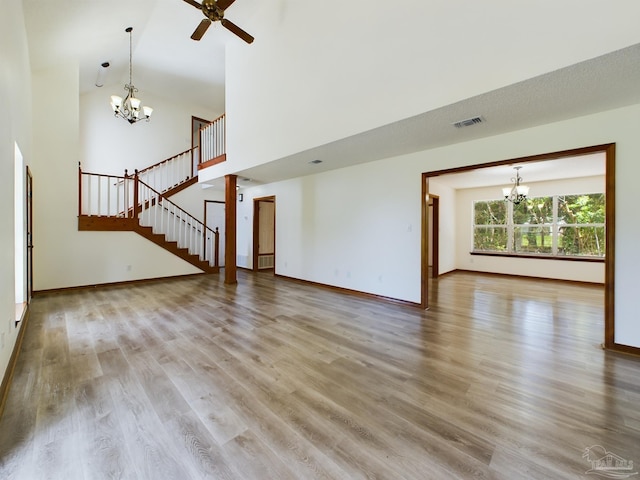 unfurnished living room featuring ceiling fan with notable chandelier, wood-type flooring, and a high ceiling