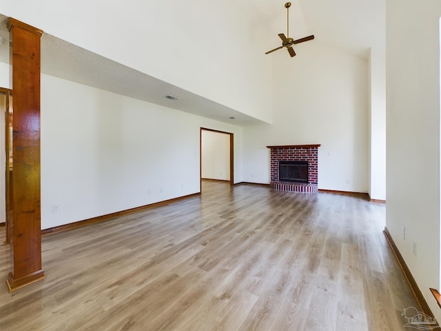 unfurnished living room with ceiling fan, a brick fireplace, high vaulted ceiling, and light hardwood / wood-style flooring