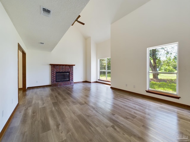 unfurnished living room with high vaulted ceiling, a textured ceiling, hardwood / wood-style flooring, ceiling fan, and a fireplace