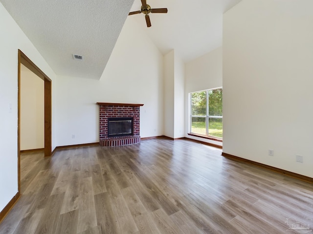 unfurnished living room with high vaulted ceiling, light wood-type flooring, ceiling fan, a brick fireplace, and a textured ceiling