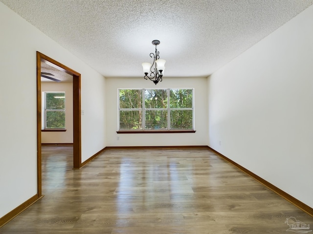 unfurnished dining area with a notable chandelier, plenty of natural light, hardwood / wood-style floors, and a textured ceiling