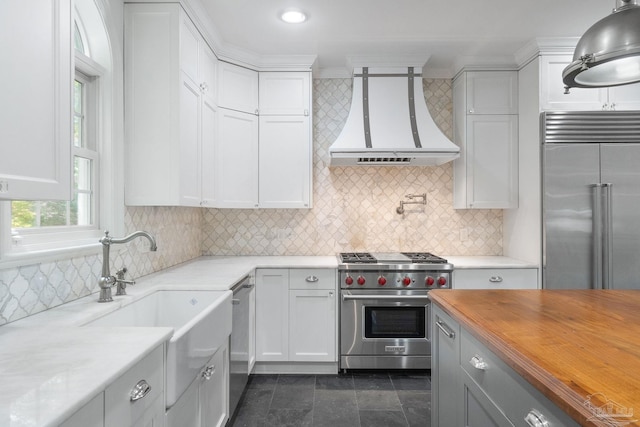 kitchen featuring a sink, custom exhaust hood, high quality appliances, and white cabinetry