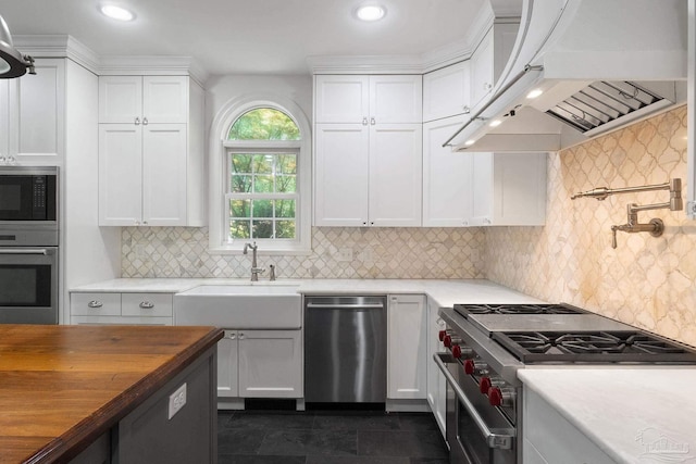 kitchen featuring appliances with stainless steel finishes, a sink, white cabinets, custom exhaust hood, and butcher block counters