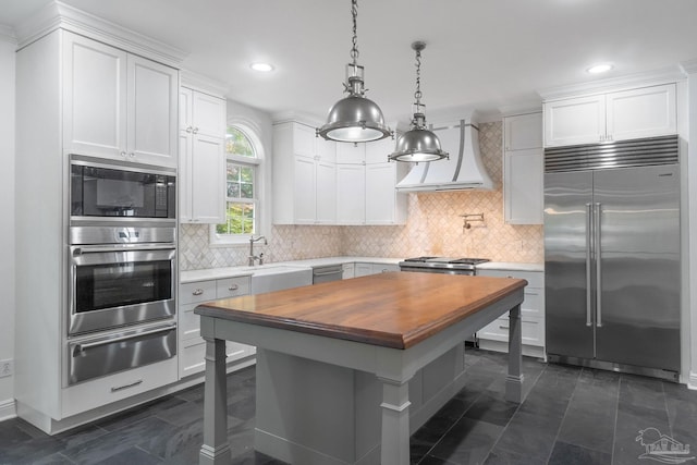 kitchen with built in appliances, custom exhaust hood, a sink, wood counters, and a warming drawer