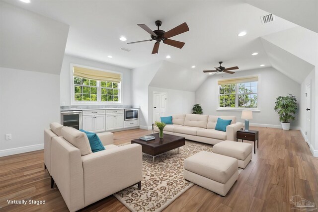 living room with a ceiling fan, light wood-style flooring, wine cooler, and vaulted ceiling