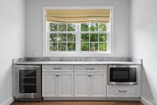 bar with beverage cooler, baseboards, built in microwave, and a healthy amount of sunlight