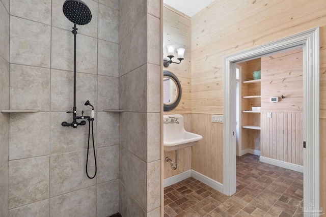 full bath with a tile shower, a sink, brick floor, wood walls, and baseboards