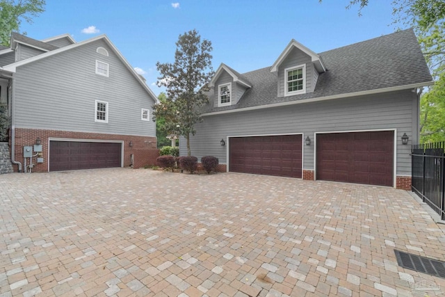 view of front facade featuring brick siding, decorative driveway, a garage, and a shingled roof