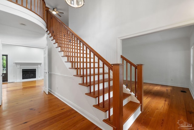 staircase featuring a ceiling fan, visible vents, a fireplace, hardwood / wood-style flooring, and baseboards