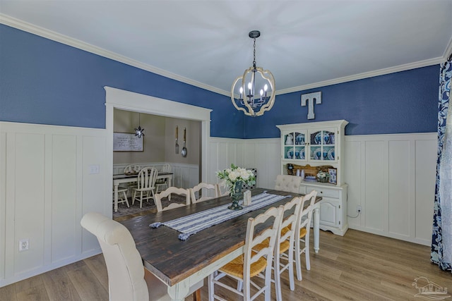 dining room with a chandelier, a wainscoted wall, crown molding, and light wood-type flooring