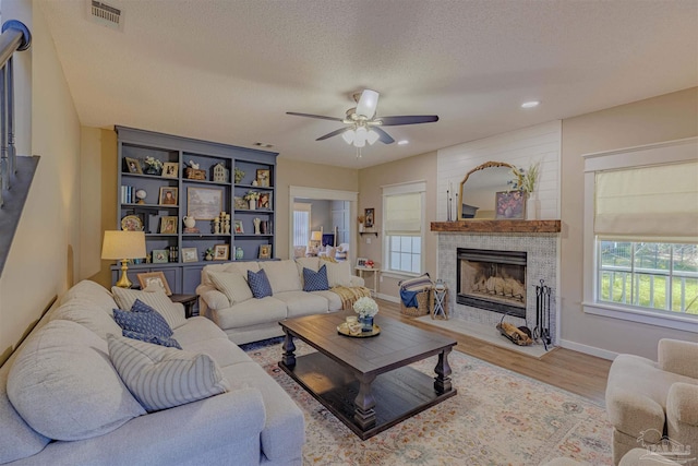 living room featuring visible vents, ceiling fan, a tiled fireplace, wood finished floors, and a textured ceiling