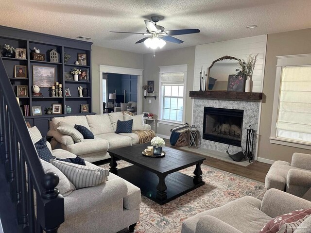 living area with wood finished floors, visible vents, ceiling fan, a stone fireplace, and a textured ceiling