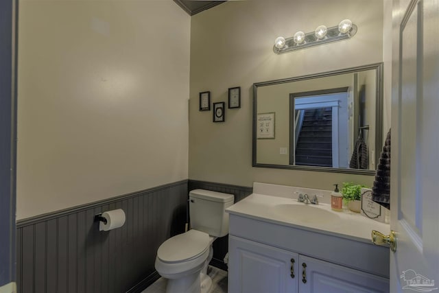 half bathroom featuring wainscoting, toilet, and vanity