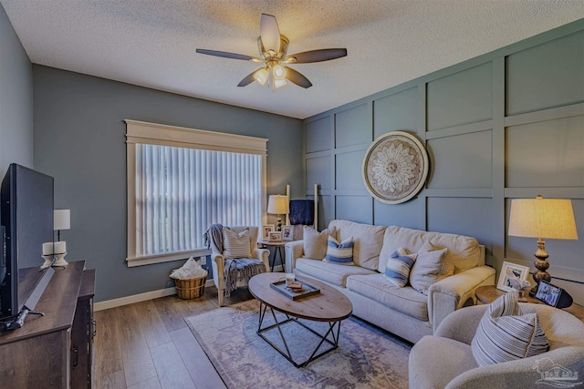 living area featuring baseboards, ceiling fan, wood finished floors, a decorative wall, and a textured ceiling