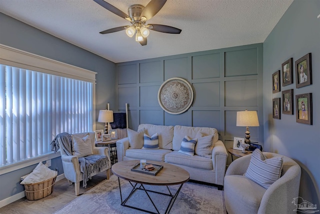 living room featuring a textured ceiling, wood finished floors, a decorative wall, baseboards, and ceiling fan
