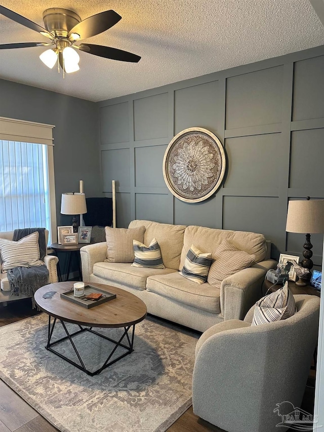 living room featuring wood finished floors, a textured ceiling, ceiling fan, and a decorative wall
