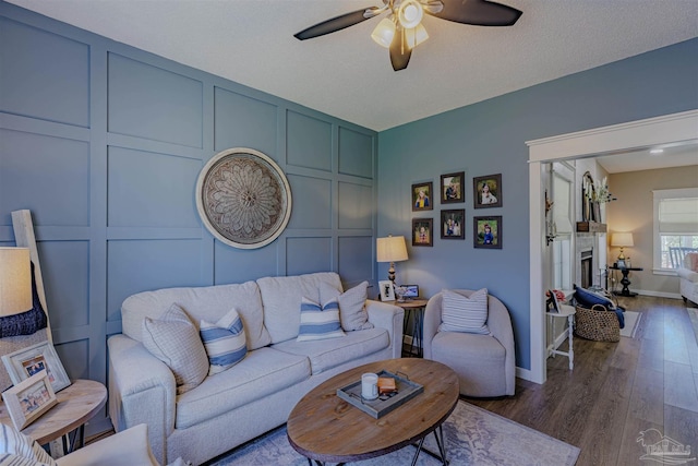 living room with a fireplace, a decorative wall, baseboards, ceiling fan, and dark wood-style flooring