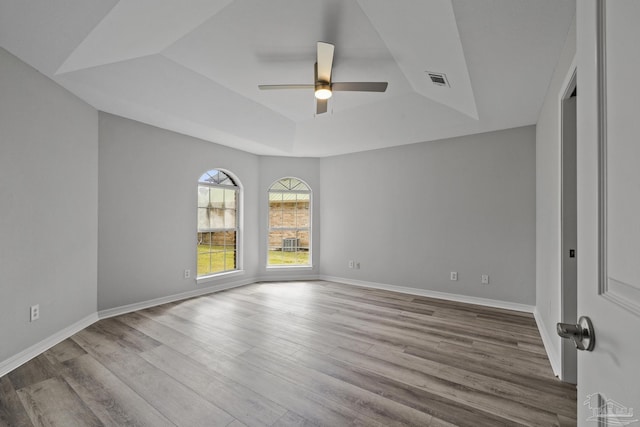 unfurnished room featuring ceiling fan, a tray ceiling, wood finished floors, and baseboards