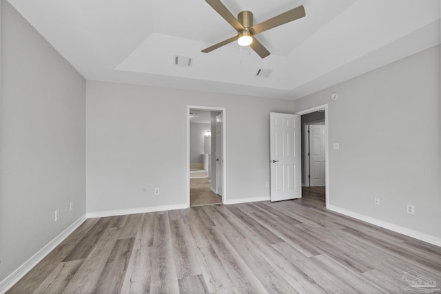 unfurnished bedroom with a tray ceiling, wood finished floors, visible vents, and baseboards