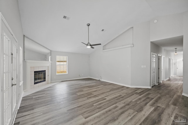 unfurnished living room with visible vents, a tiled fireplace, ceiling fan, wood finished floors, and baseboards