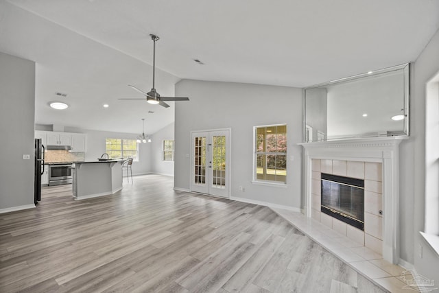 unfurnished living room with light wood finished floors, visible vents, vaulted ceiling, a tile fireplace, and ceiling fan with notable chandelier