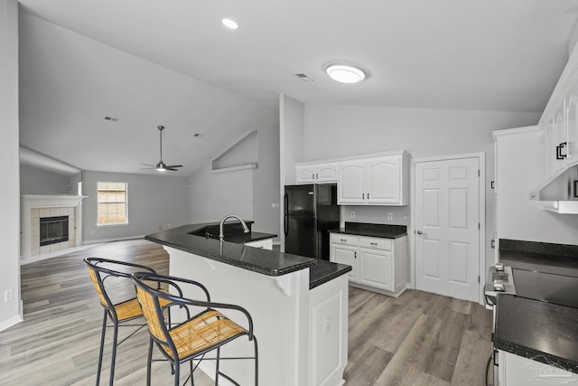 kitchen featuring a breakfast bar, a tiled fireplace, freestanding refrigerator, stainless steel range with electric cooktop, and white cabinetry