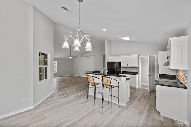 kitchen featuring a breakfast bar, freestanding refrigerator, white cabinetry, and dark countertops