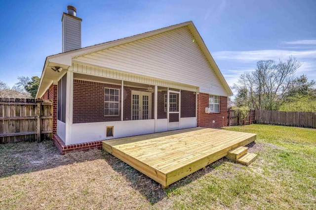 back of property featuring a deck, a fenced backyard, brick siding, a lawn, and a chimney