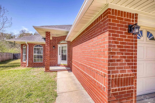 doorway to property featuring a garage, brick siding, a shingled roof, fence, and a yard