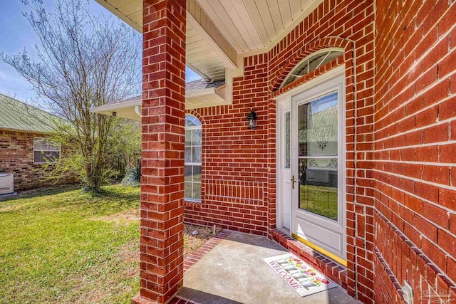 view of exterior entry featuring brick siding and a yard