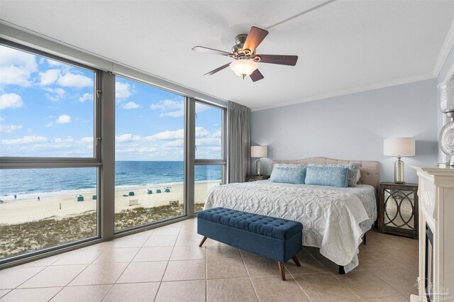 tiled bedroom featuring floor to ceiling windows, a view of the beach, crown molding, a water view, and ceiling fan