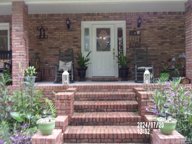 view of exterior entry featuring a porch and brick siding