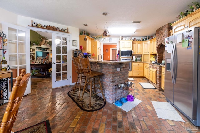 kitchen featuring light brown cabinets, brick floor, a peninsula, and stainless steel appliances