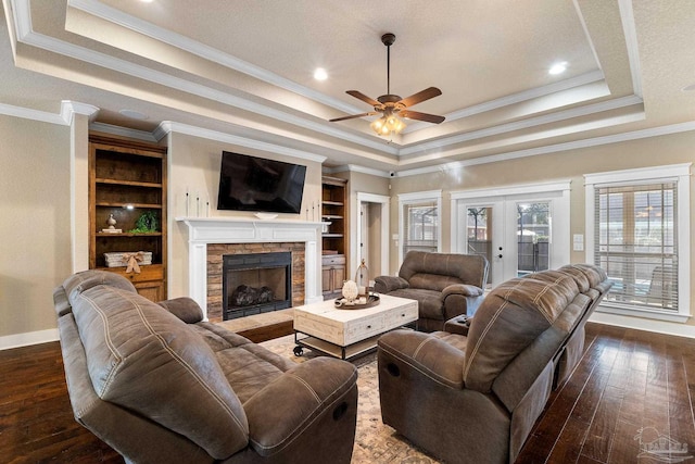 living room featuring ceiling fan, dark wood-type flooring, a raised ceiling, a fireplace, and ornamental molding