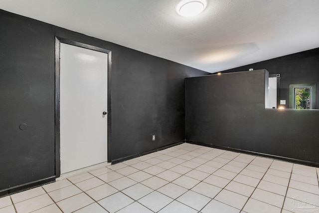 unfurnished room with vaulted ceiling, a textured ceiling, and light tile patterned floors