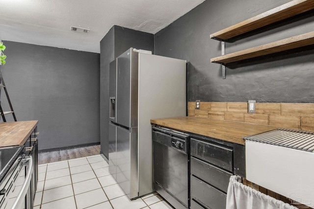 kitchen featuring stainless steel appliances, a textured ceiling, butcher block countertops, and light tile patterned flooring