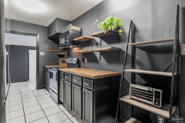 kitchen with electric range oven, butcher block countertops, and light tile patterned floors