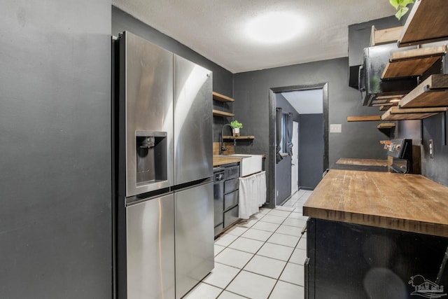 kitchen featuring sink, light tile patterned floors, a textured ceiling, black appliances, and butcher block counters