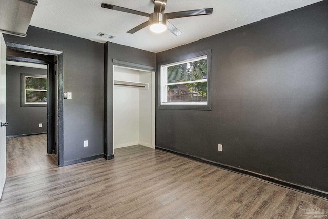 unfurnished bedroom featuring a closet, multiple windows, hardwood / wood-style flooring, and ceiling fan