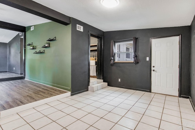 foyer featuring vaulted ceiling with beams, light hardwood / wood-style floors, and a textured ceiling