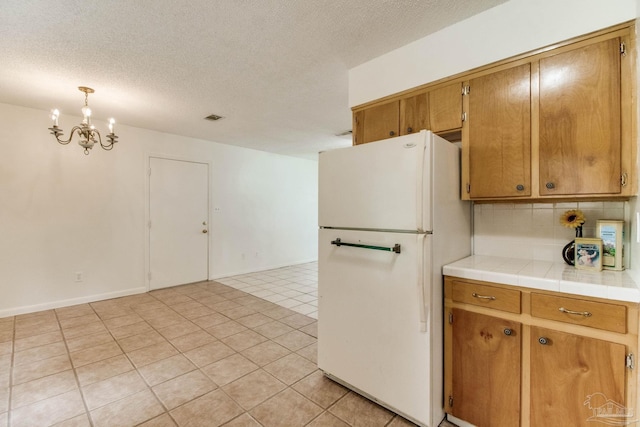 8500 Blue Jay Way, Pensacola, FL 32534 - kitchen featuring freestanding refrigerator, a chandelier, a textured ceiling, decorative backsplash, and tile counters