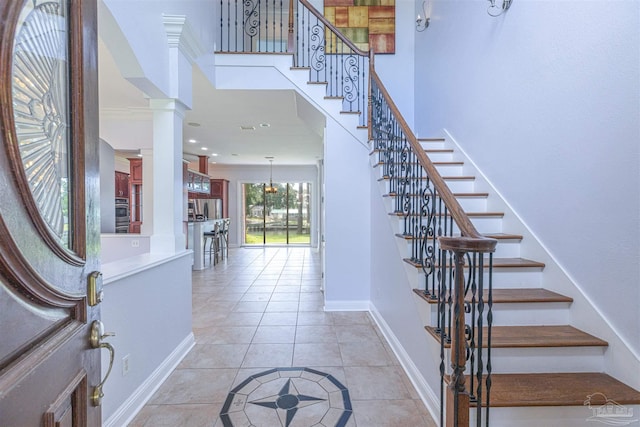 foyer with ornate columns, light tile patterned flooring, and ornamental molding