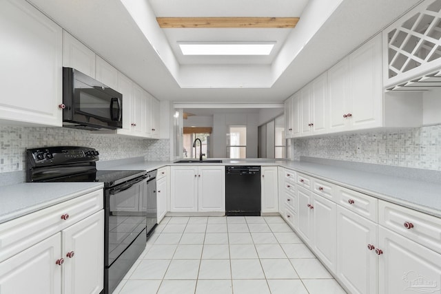 kitchen with a skylight, white cabinets, light tile patterned floors, sink, and black appliances