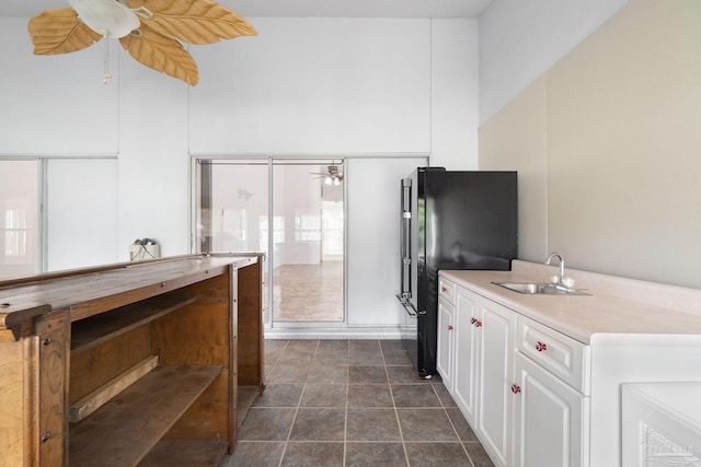 kitchen with dark tile patterned flooring, black refrigerator, sink, ceiling fan, and white cabinets